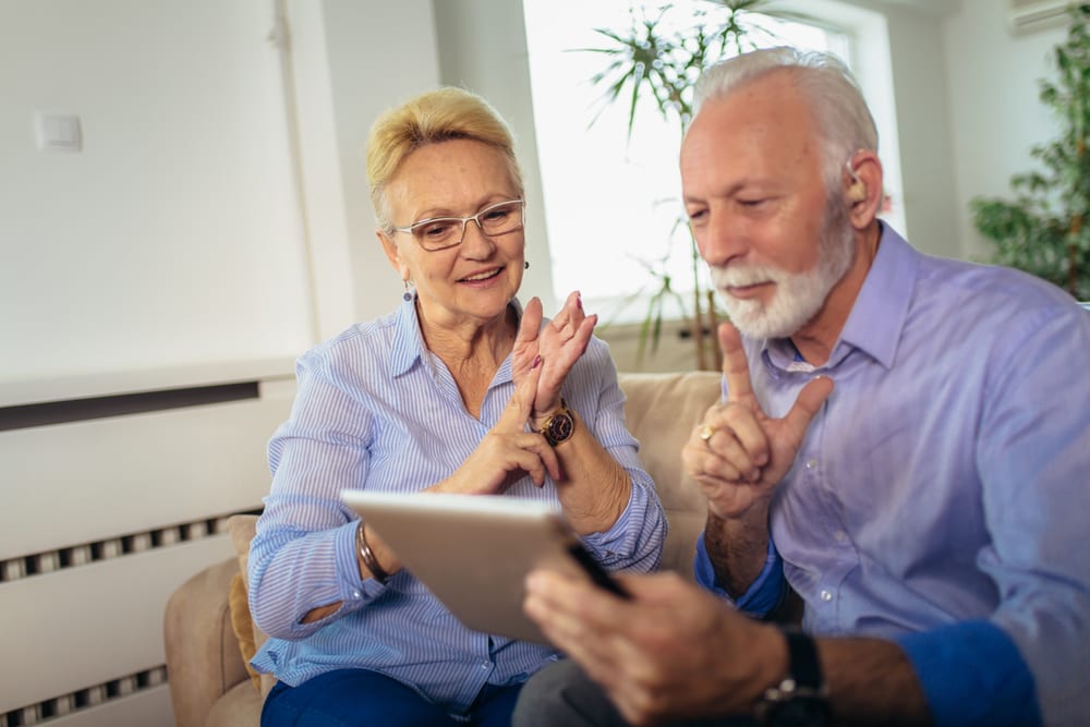 Couple de seniors souriants regardant une tablette sur un canapé