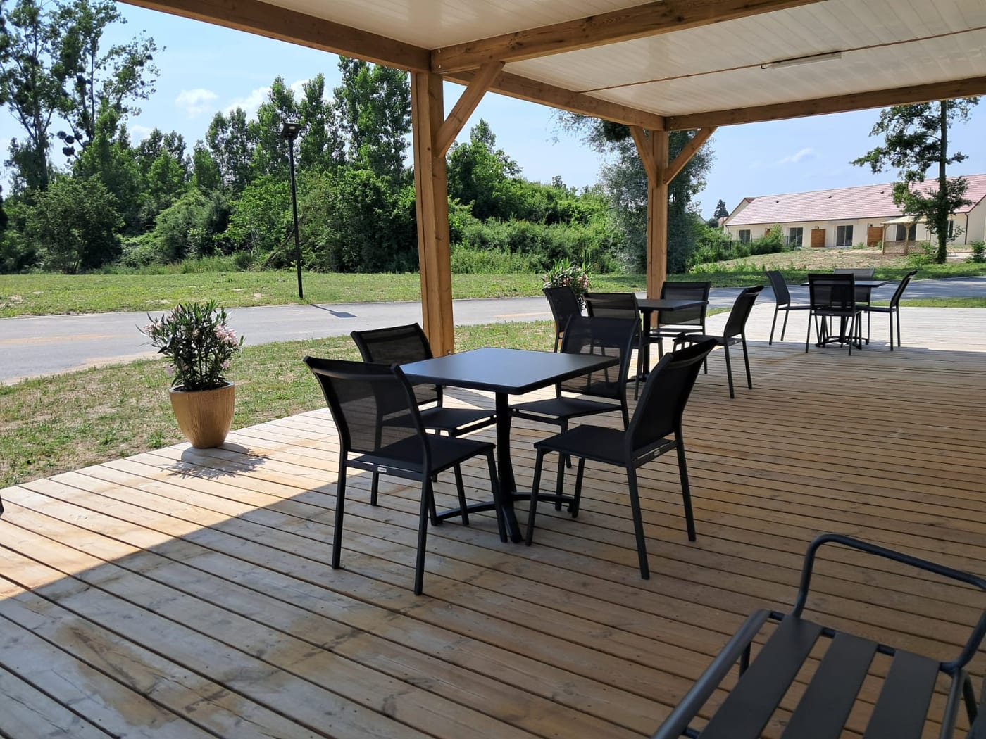 Terrasse en bois sous pergola avec tables et chaises, village Sérénya